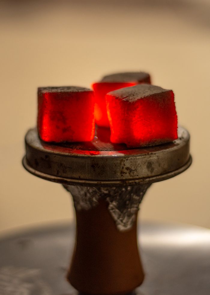 Close-up of glowing red charcoal cubes on a hookah setup, indoors.